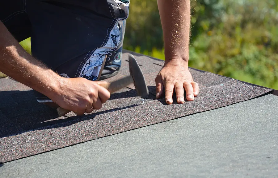 Close up of a male roofer installing asphalt shingles on a roof. 