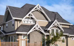 Large, 2-story tan home with a newer asphalt roof against a blue sky. 